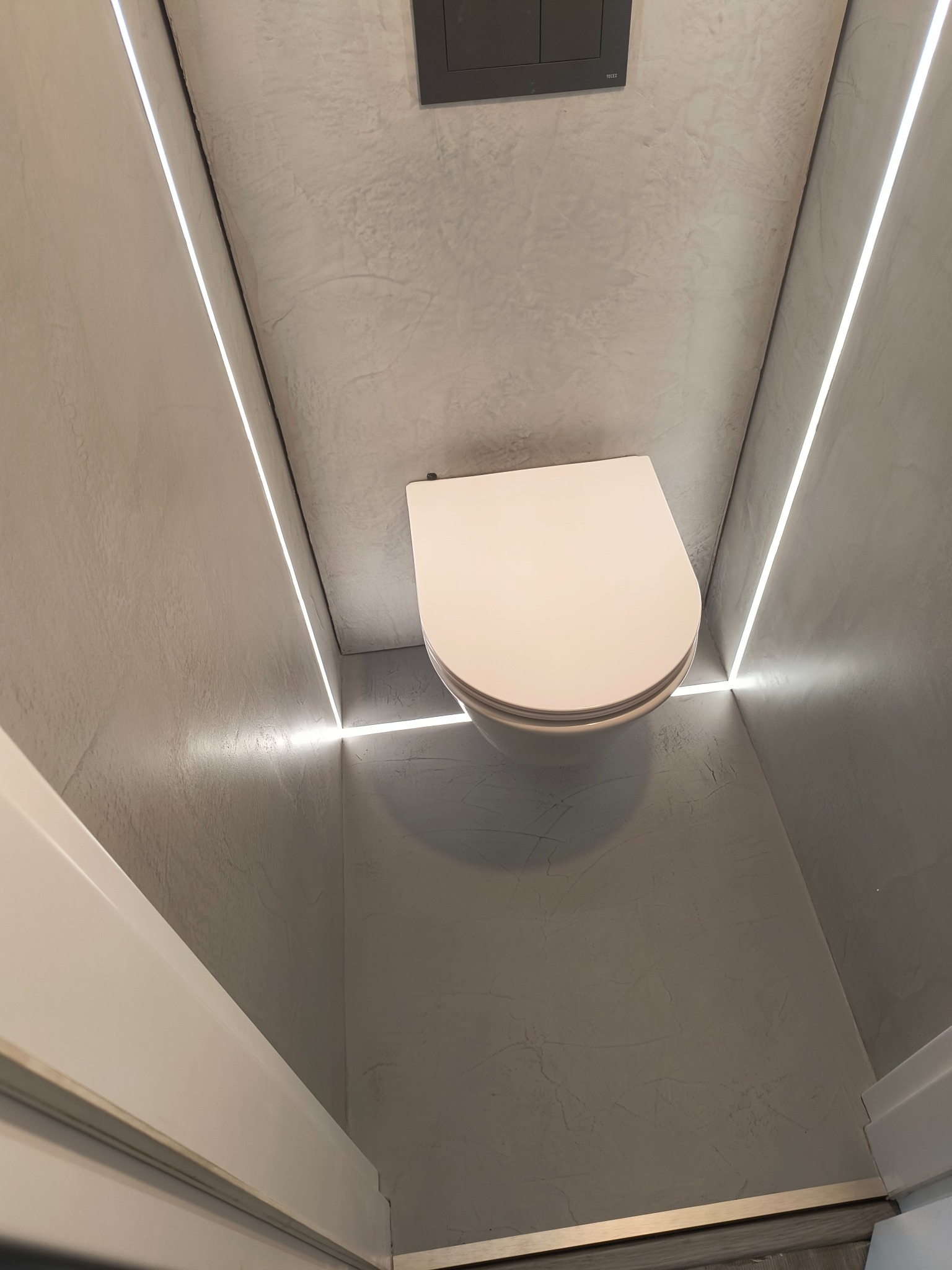 Nowoczesna toaleta w Ustroniu z oświetleniem LED wzdłuż ścian wykończonych w szarości, minimalistyczny design i czysta forma.