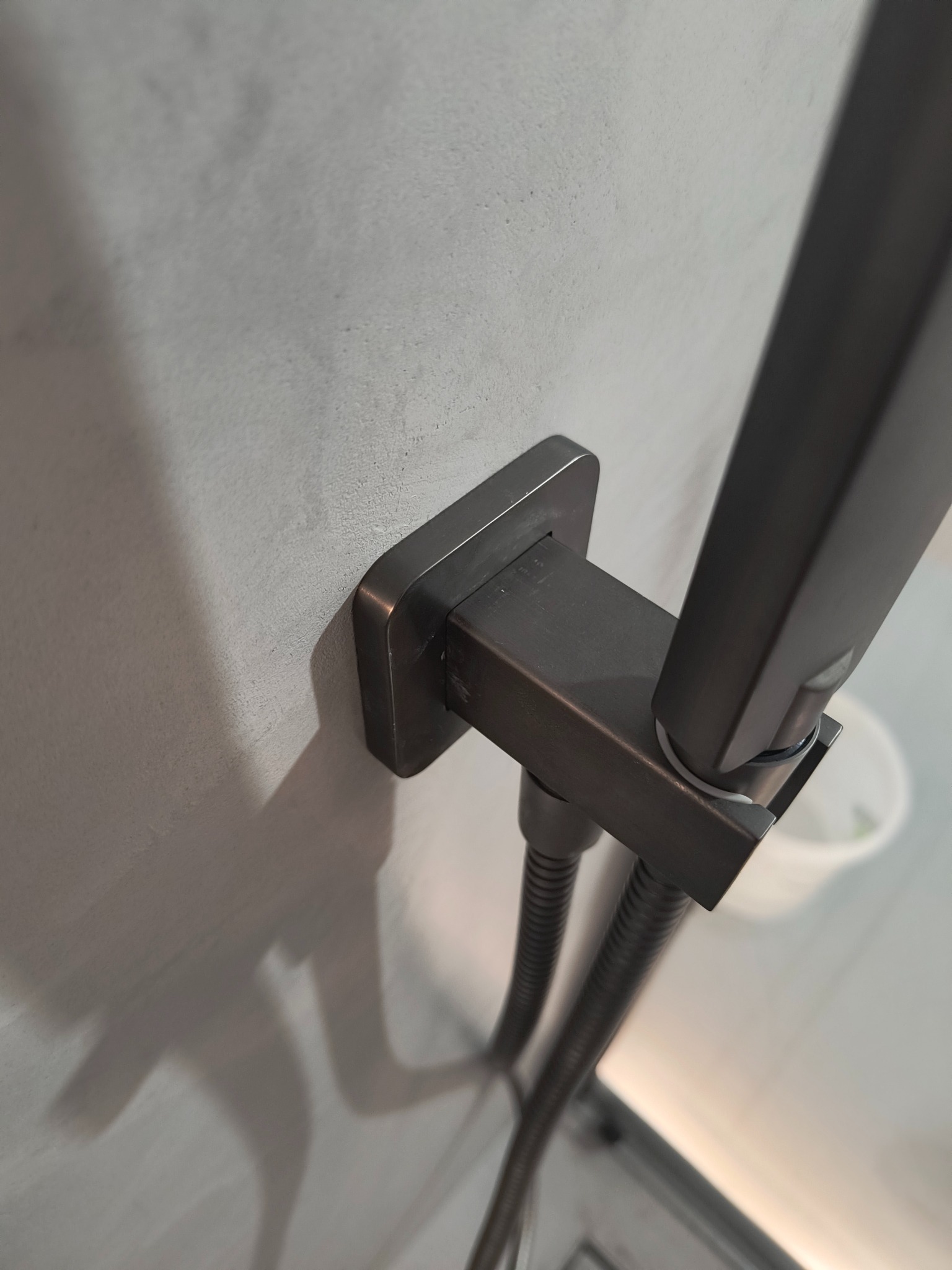 Szczegółowy widok na nowoczesną, grafitową słuchawkę prysznicową zamontowaną na jasnej, matowej ścianie. Minimalistyczny design i precyzyjne wykończenie.