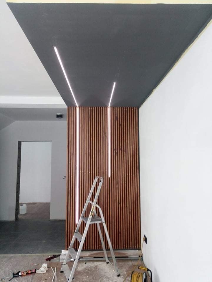 Szara, pomalowana część sufitu z wbudowanym oświetleniem LED nad drewnianą ścianą działową z listew, widoczna drabina i narzędzia malarskie na podłodze w trakcie prac wykończeniowych.