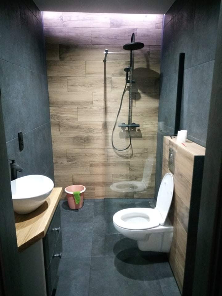 Nowoczesna łazienka z ciemnymi płytkami i elementami drewna, z kabiną prysznicową typu walk-in i umywalką nablatową.