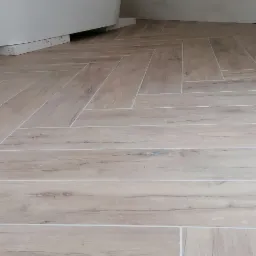 Ułożona pod kątem jasna podłoga z płytek imitujących drewno w łazience, widoczny fragment wanny.