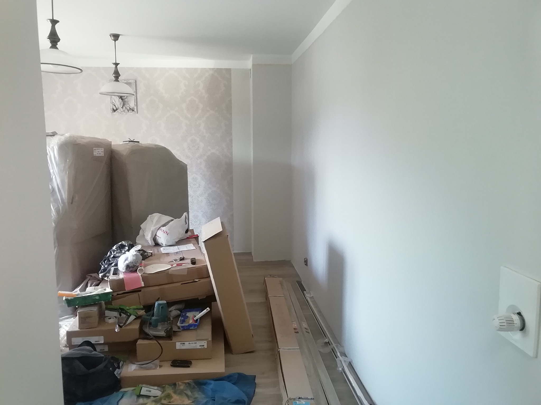 Przygotowania do remontu pokoju w Giżycku: kartony, narzędzia i materiały budowlane zgromadzone w pomieszczeniu z nowymi panelami podłogowymi i świeżo pomalowaną ścianą.