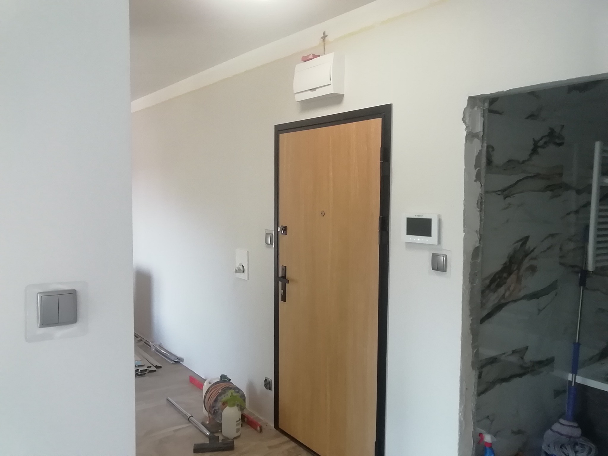 Wnętrze mieszkania w trakcie prac wykończeniowych: widoczna nowa drewniana stolarka drzwiowa z czarną ramą, fragment wykończonej łazienki z marmurowymi płytkami oraz narzędzia i materiały budowlane...