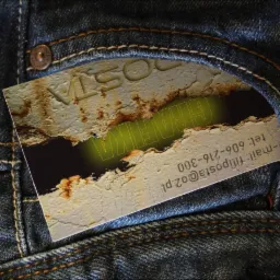 Wizytówka z efektem zniszczonej ściany i zielonym napisem 'GRAFIKA' wystająca z kieszeni dżinsów.