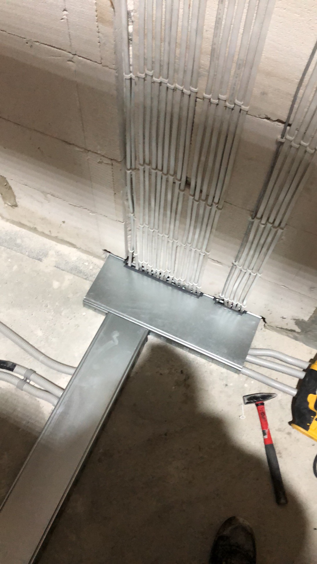 Szereg rurek elektroinstalacyjnych prowadzonych w ścianie z betonu komórkowego, z puszką rozdzielczą i korytem kablowym; widoczny młotek i wiertarka akumulatorowa.