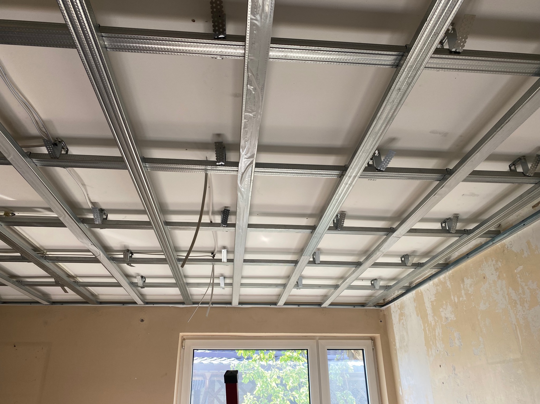 Sufit podwieszany z metalową konstrukcją w trakcie montażu, widok z dołu. Realizacja z Białystoku, widoczne profile i płyty. Część profili w folii ochronnej.