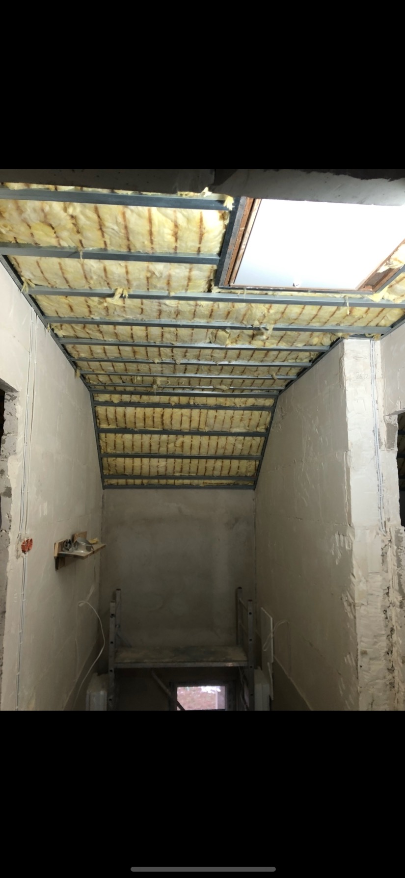 Ocieplenie stropu wełną mineralną w metalowej konstrukcji. Widoczne niedokończone ściany, surowy stan wnętrza. Prace remontowe w toku.