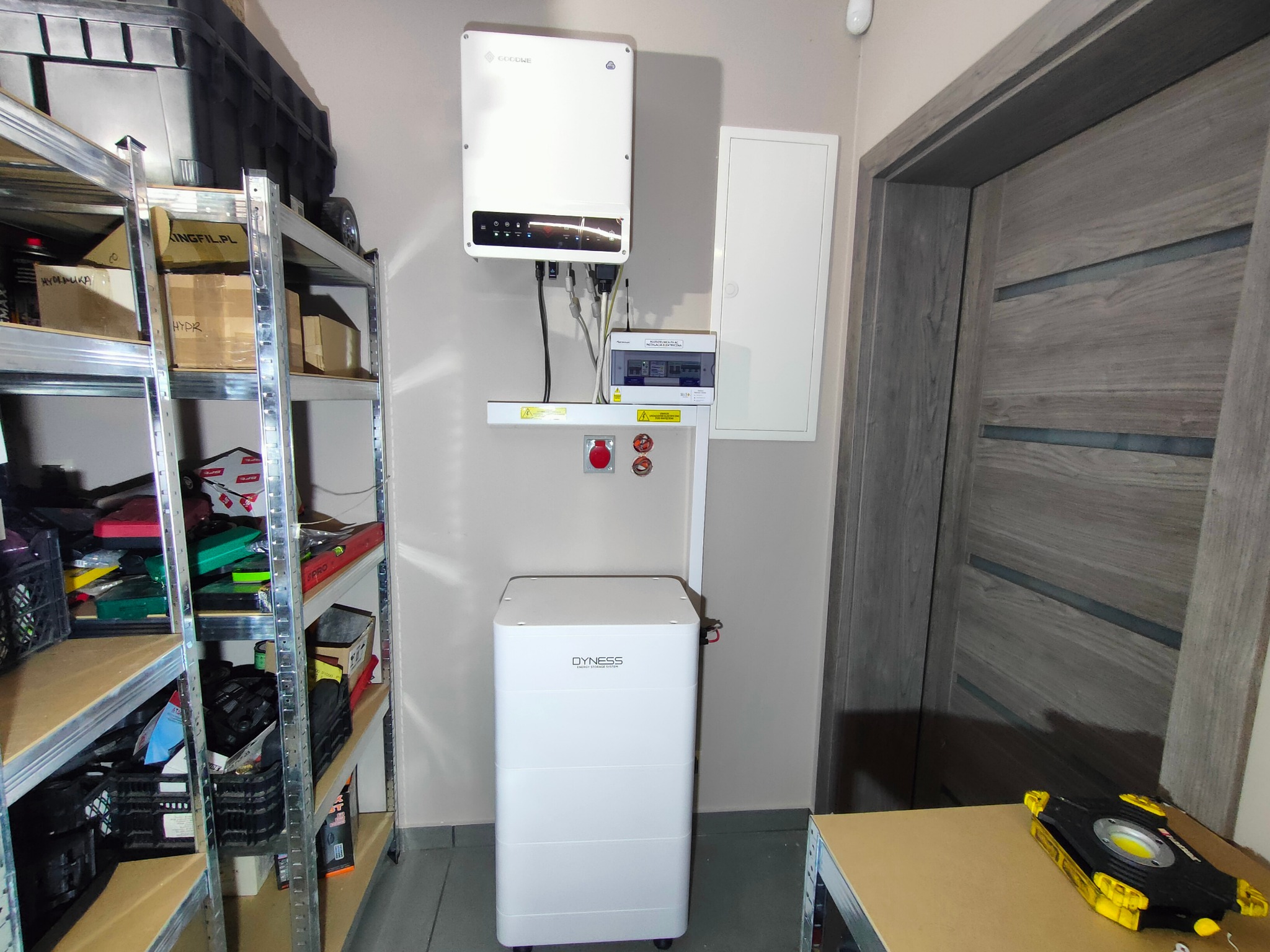 Kompletna instalacja fotowoltaiczna w pomieszczeniu: inwerter GoodWe, bateria Dyness, rozdzielnica. Widoczny regał z narzędziami.