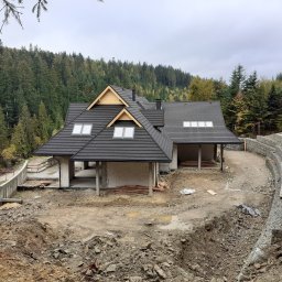 WiBud Wiesław Górka - Budynek w stanie surowym otwartym z czarnym dachem, widoczna konstrukcja murowana i teren w trakcie prac ziemnych, w tle las.