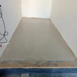 Przygotowany podkład podłogowy z listwą przyścienną, widoczne kable elektryczne wystające ze ściany.