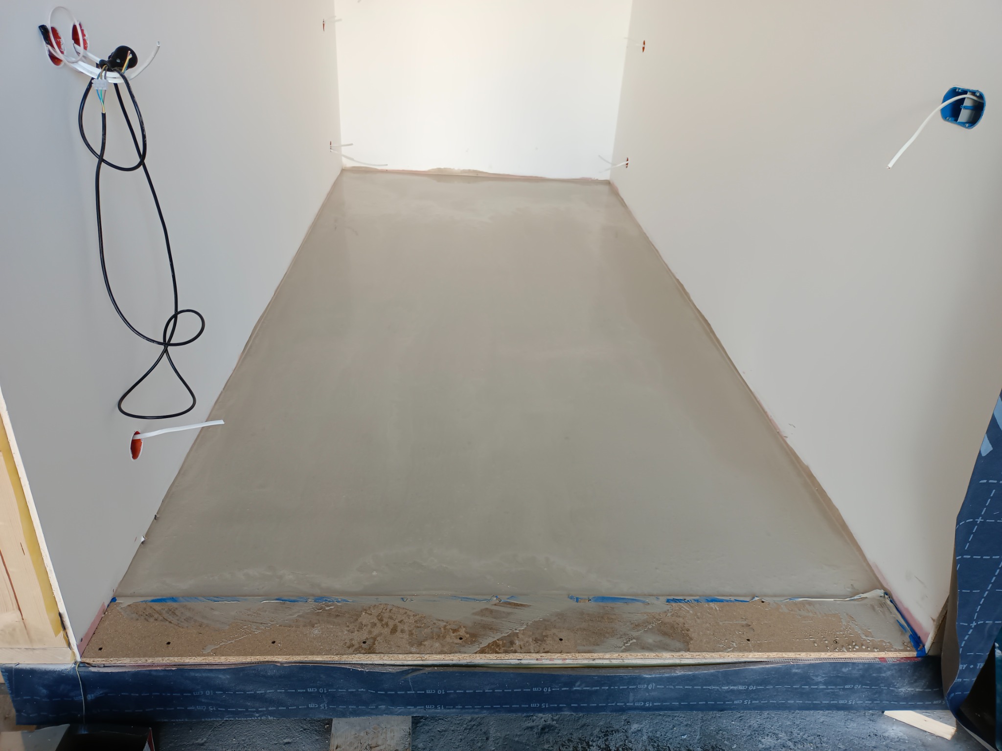 Przygotowany podkład podłogowy z listwą przyścienną, widoczne kable elektryczne wystające ze ściany.