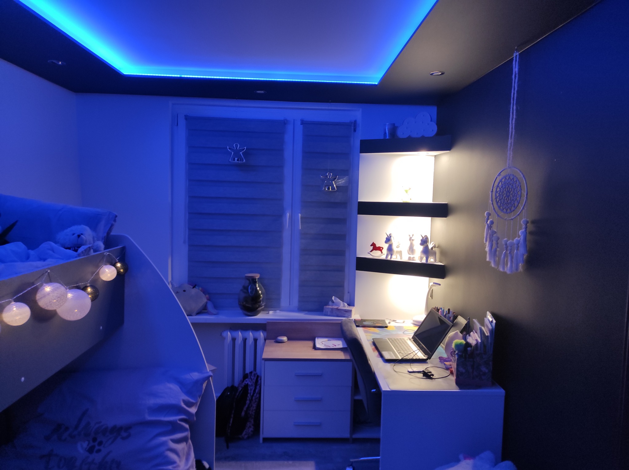 Pokój dziecięcy z łóżkiem piętrowym, biurkiem i oświetleniem LED w kolorze niebieskim, widoczne dekoracje okienne i półki z ozdobami.