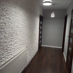 R-BUD - Korytarz z białymi płytkami imitującymi kamień na ścianie, ciemnymi panelami podłogowymi i dwoma nowoczesnymi lampami wiszącymi.