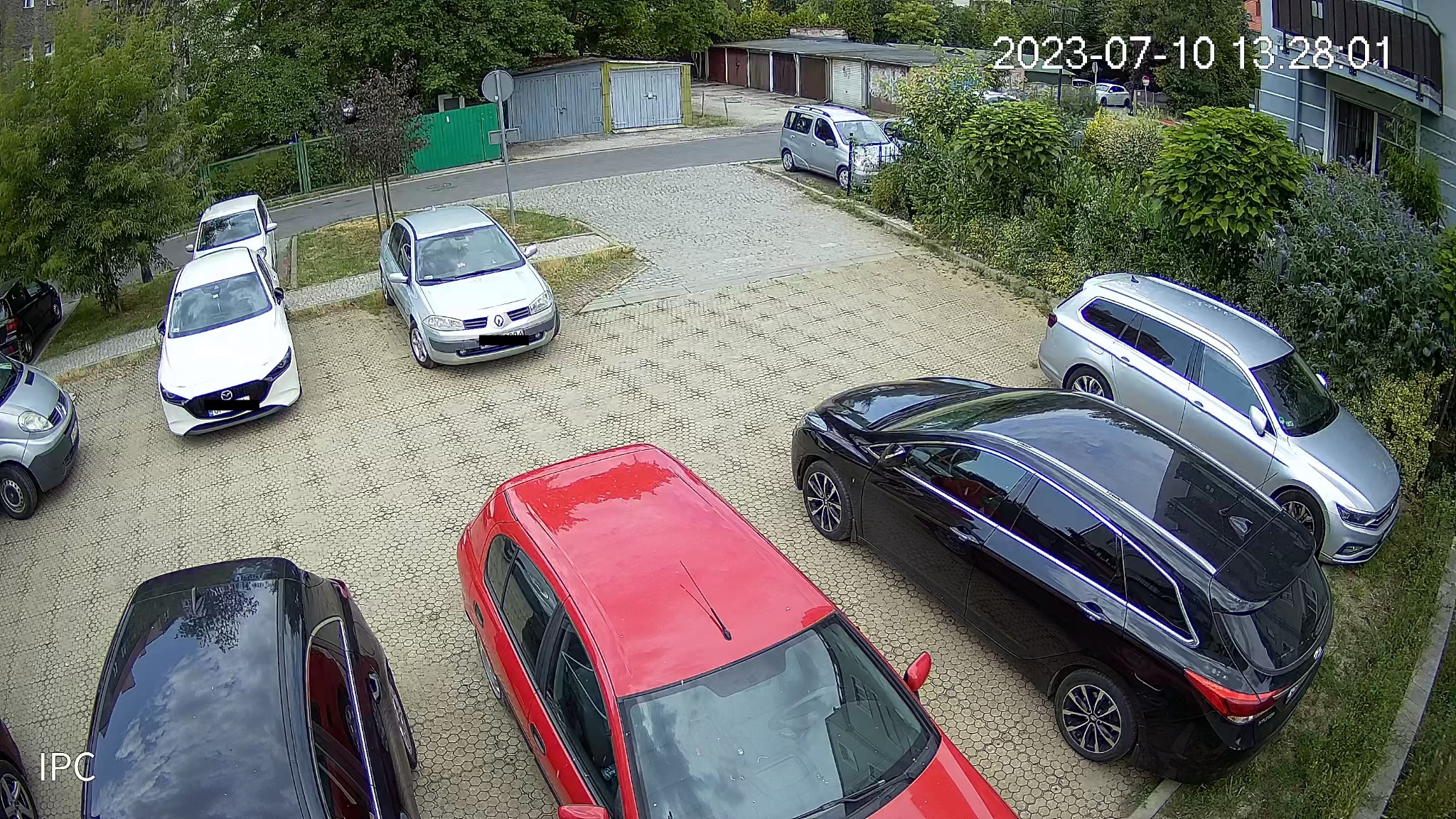 Widok z kamery na osiedlowy parking z zaparkowanymi samochodami w różnych kolorach, zarejestrowany 10 lipca 2023 roku.