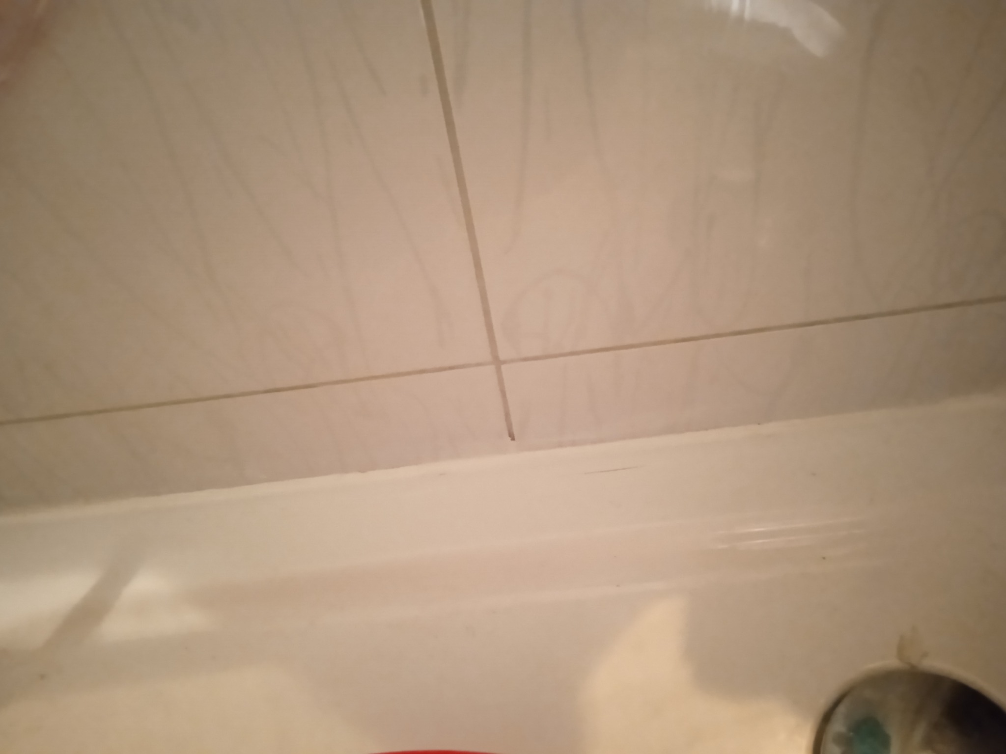 Jasne, kwadratowe płytki ułożone na ścianie nad białą wanną, widoczne fugi i fragment armatury.