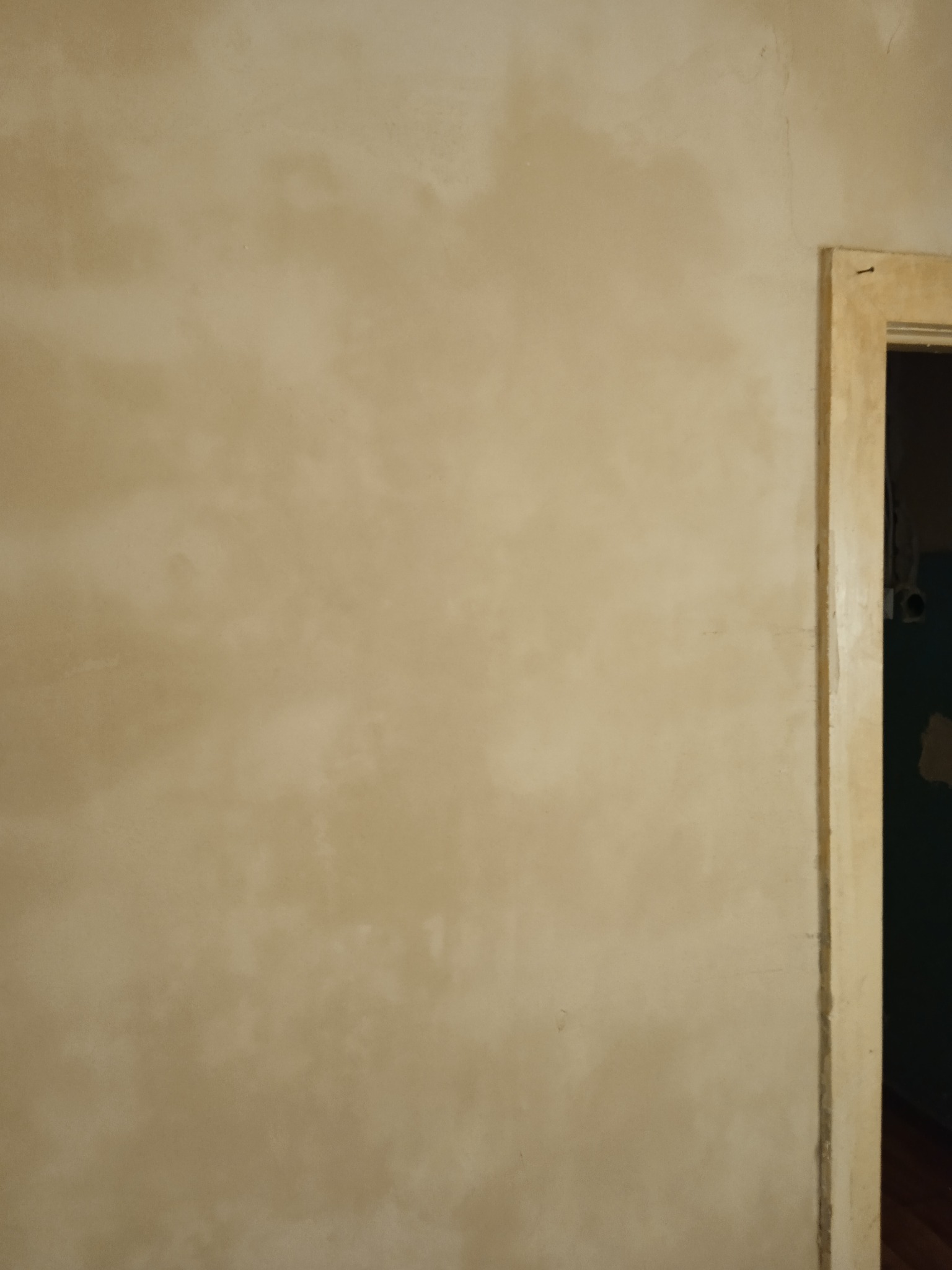 Beżowa ściana po szpachlowaniu, z widoczną fakturą i fragmentem ościeżnicy drzwiowej po prawej stronie.