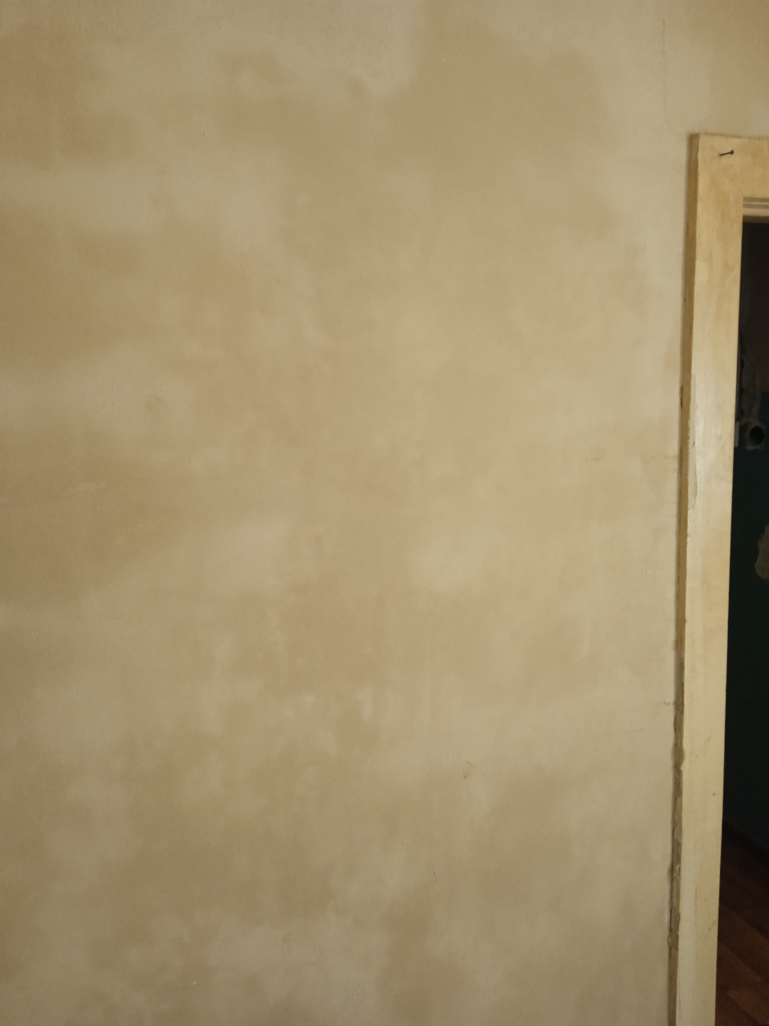 Ściana po szpachlowaniu, z widocznymi śladami po nałożeniu gładzi, przygotowana do malowania; widoczna ościeżnica drzwi.