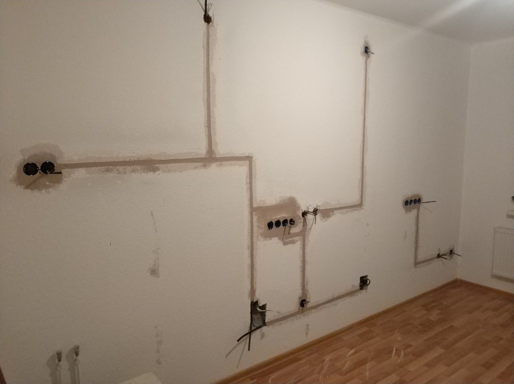 Ściana w trakcie przygotowania do malowania z wyżłobieniami na kable elektryczne i puszkami pod gniazdka, widoczne przewody