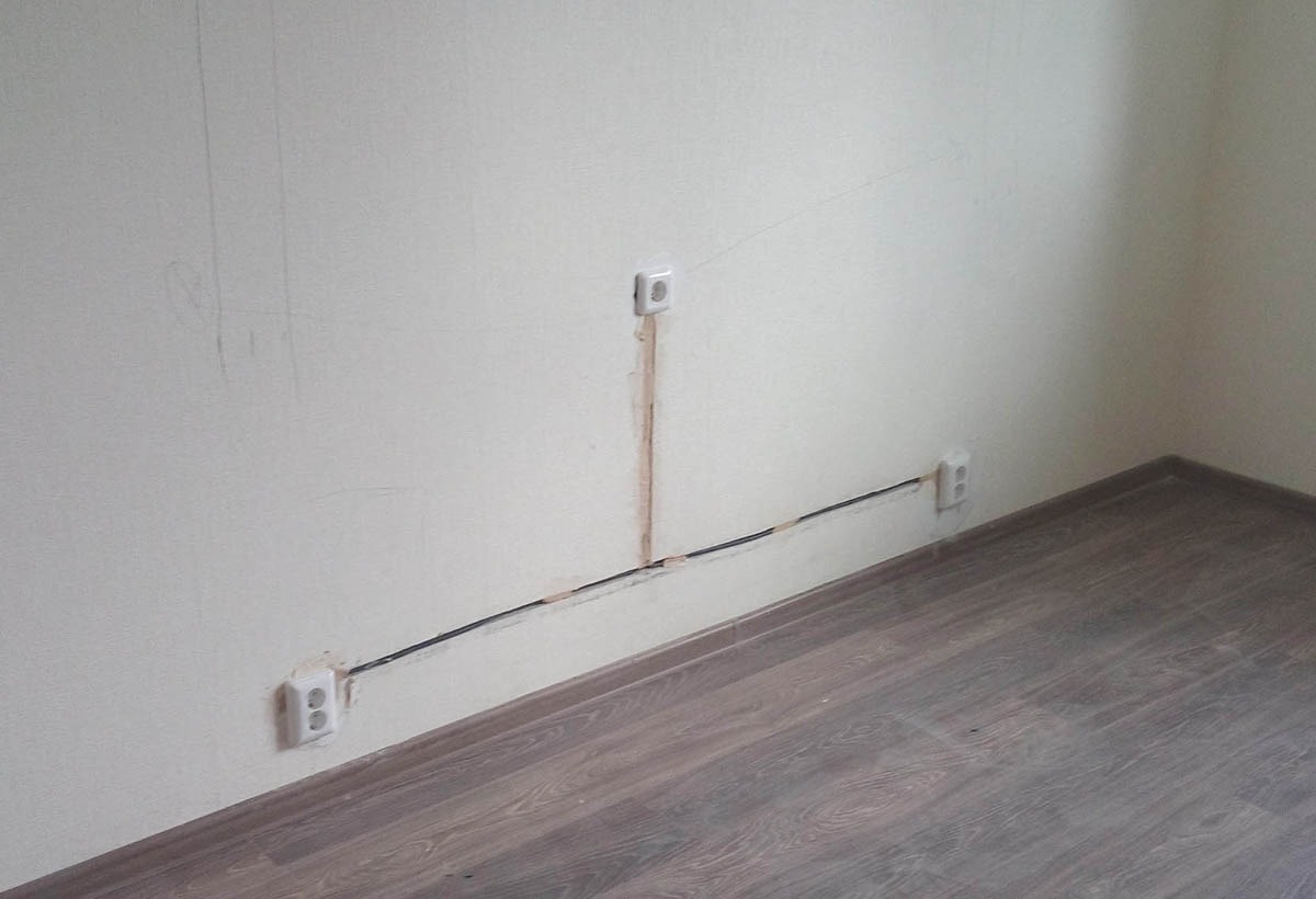 Ściana z widocznymi, nowo poprowadzonymi przewodami elektrycznymi w bruzdach i gniazdkami, przygotowana do szpachlowania, z widocznymi śladami ołówka na ścianie.