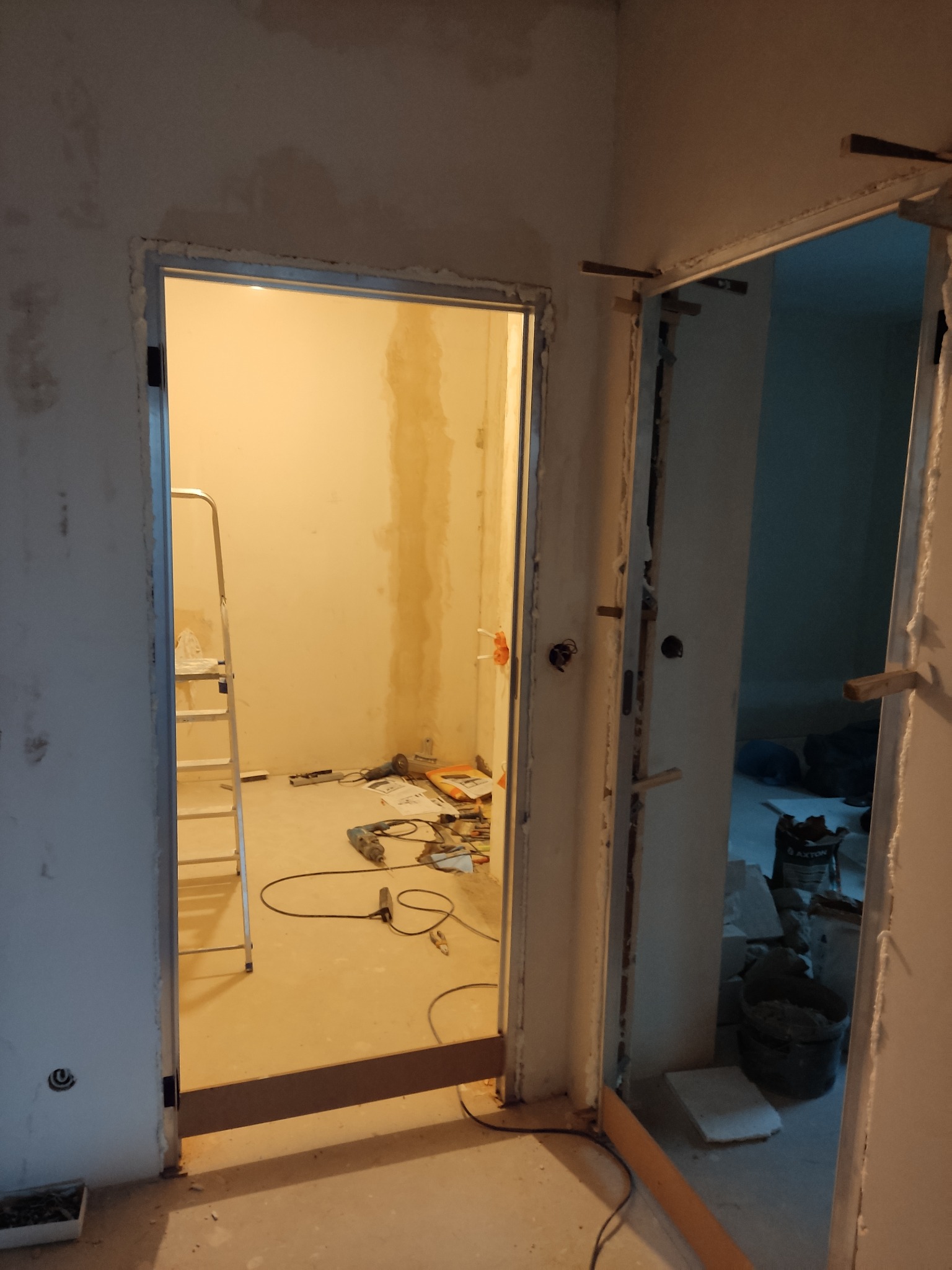 Demontaż ościeżnicy: widok na dwa otwory drzwiowe w trakcie remontu, z widocznymi narzędziami, drabiną i przygotowanymi ścianami.