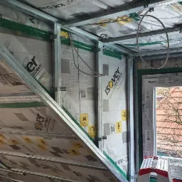 Poddasze w trakcie ocieplania w Police: widoczne profile metalowe, izolacja Isover z folią, okno Drutex i drabina. Prace izolacyjne na ukośnej ścianie.