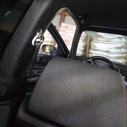 Krystian Michałowski - Wnętrze samochodu z nową, czarną podsufitką z przeszyciami w romby, widoczny słupek z obszyciem, zagłówek i kierownica. W tle przez okno widoczne worki z nieznaną zawartością.