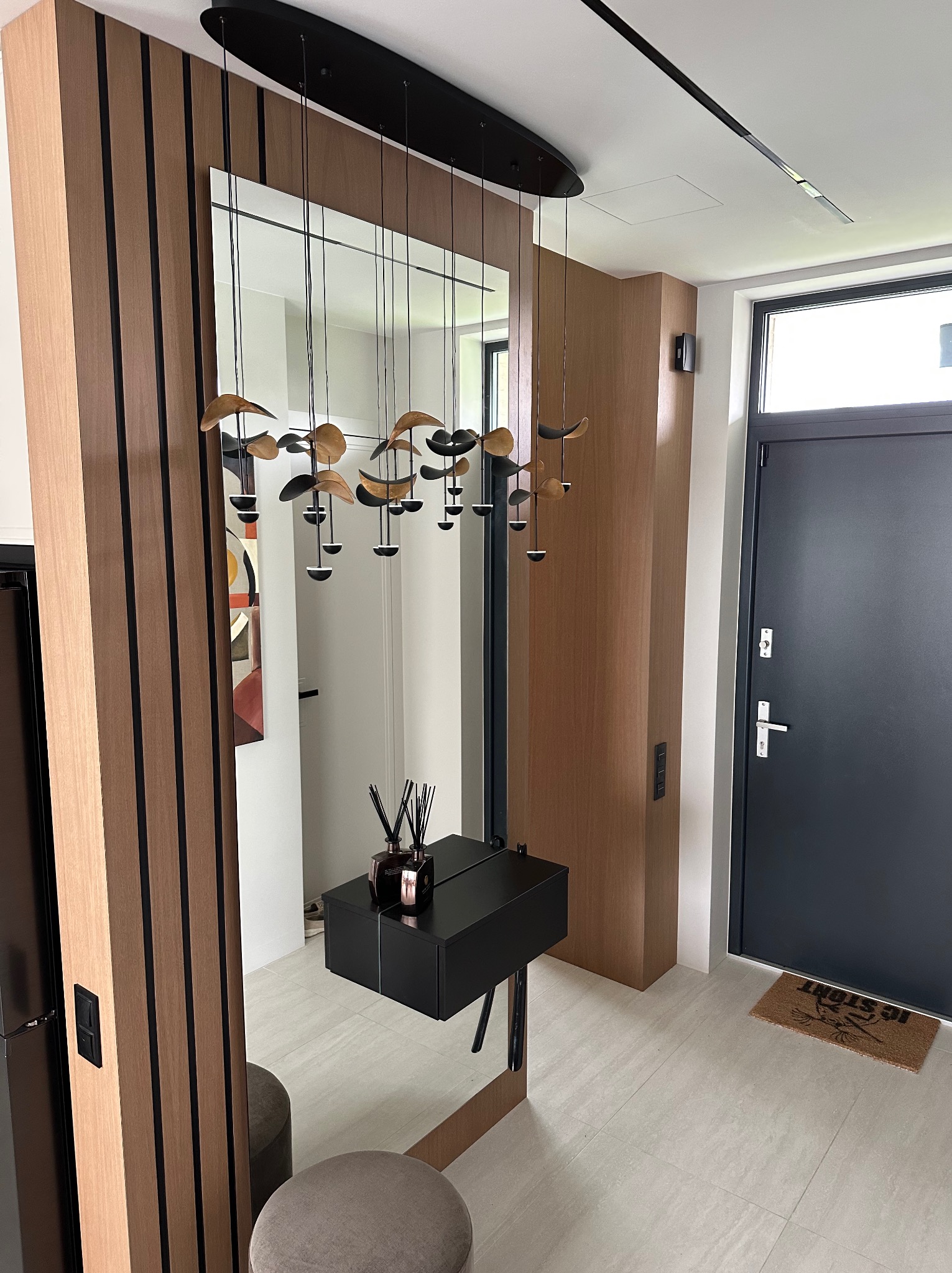 Nowoczesny przedpokój z lustrem i drewnianą zabudową. Uwagę przyciąga designerska lampa wisząca i minimalistyczna konsola z czarnym blatem.