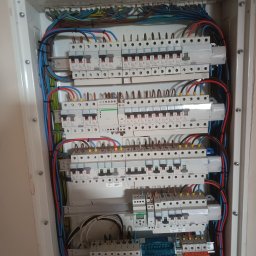 Electro Wit-Bud Michał Witczak - Rozdzielnica elektryczna z zainstalowanymi bezpiecznikami, przewodami oznaczonymi kolorami i elementami zabezpieczającymi, zamontowana w białej obudowie w trakcie prac instalacyjnych.