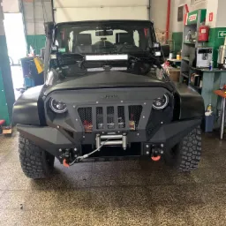 Czarny Jeep Wrangler z tuningowanym przednim zderzakiem, osłoną chłodnicy i dodatkowym oświetleniem LED w warsztacie.