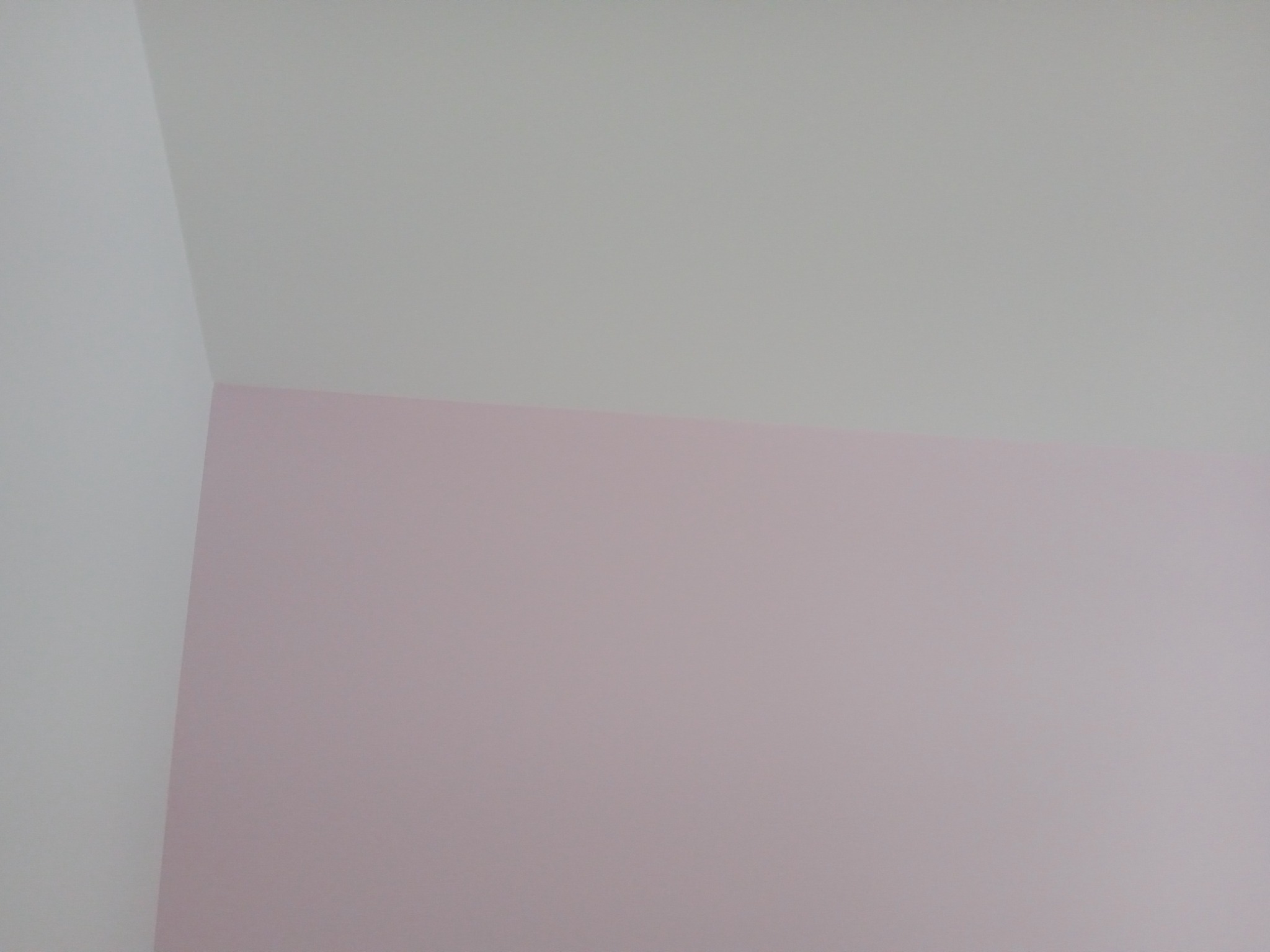 Ściana w rogu pokoju, pomalowana w górnej części na biało, a w dolnej na delikatny róż, z widocznym załamaniem sufitu.