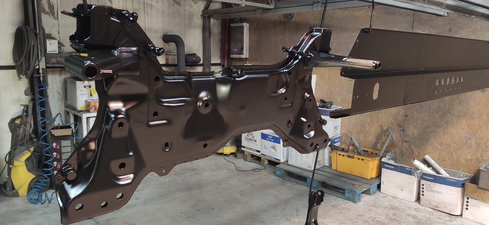 Metalowa rama samochodowa po malowaniu proszkowym na czarno, zawieszona w warsztacie, widoczne elementy konstrukcyjne i otwory montażowe.