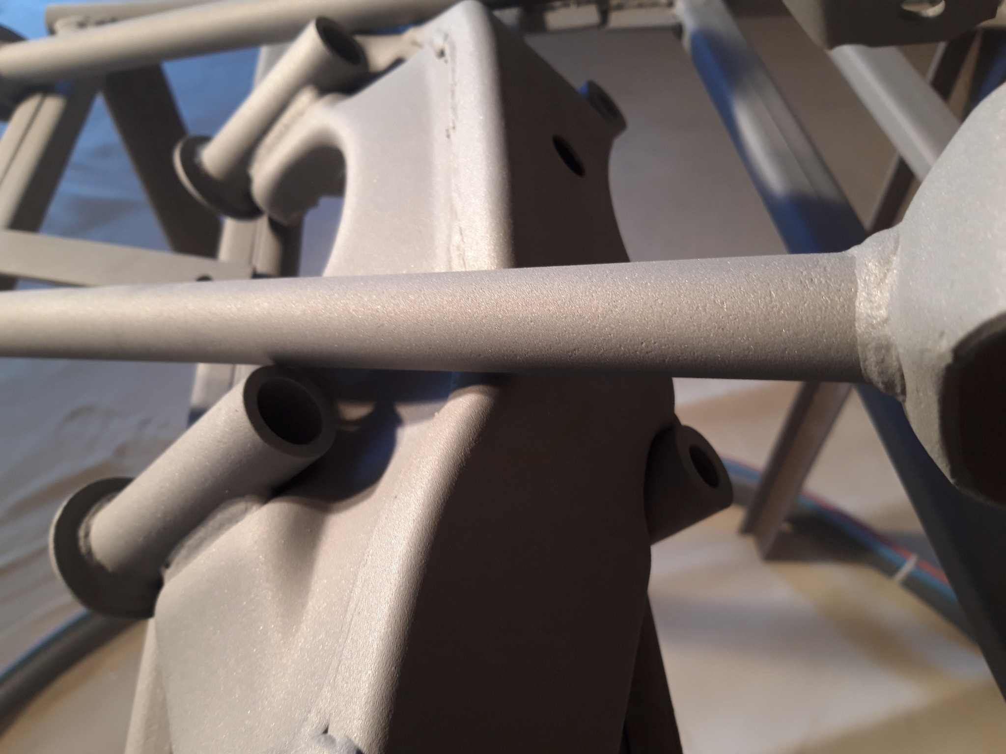 Szare, metalowe elementy konstrukcyjne po obróbce, widoczne otwory i spawy, matowe wykończenie.