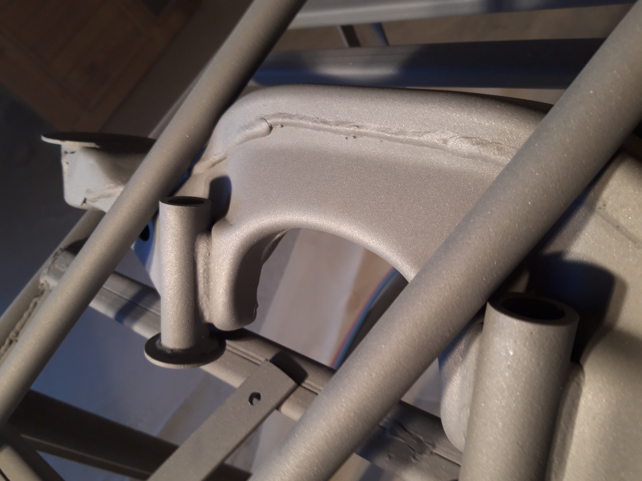 Szczegół ramy pojazdu po obróbce, pokrytej jednolitą, szarą powłoką o matowej teksturze, widoczne ślady spawania i otwory montażowe.