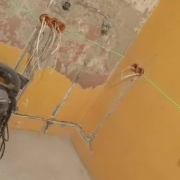 Wnętrze w trakcie prac elektrycznych: widoczne przewody wystające ze ścian i sufitu, wyznaczane laserowo linie poziome, surowe ściany w trakcie remontu, butelki po napojach na podłodze.