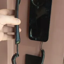 Czarny domofon z kablem spiralnym zamontowany na różowej ścianie, trzymany w dłoni podczas instalacji.