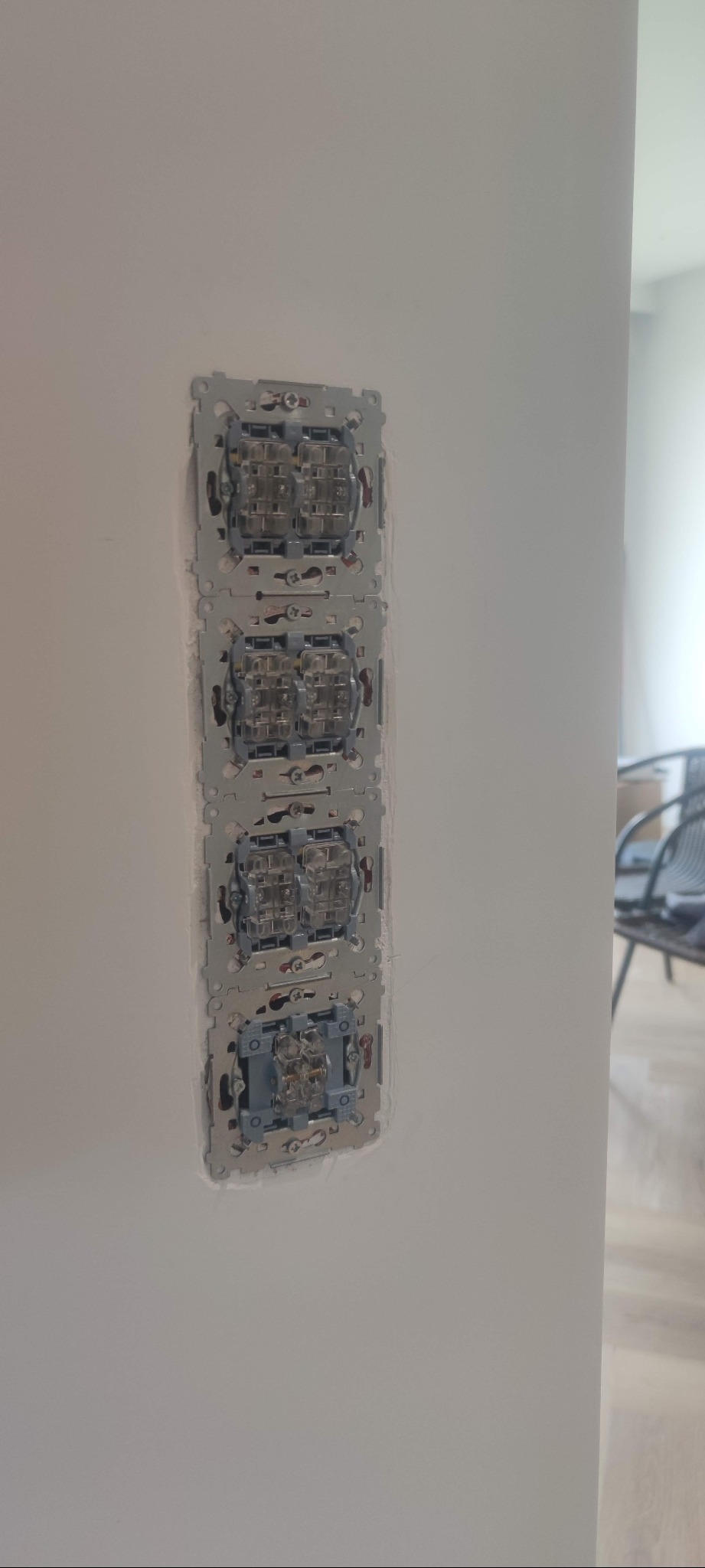 Cztery puszki podtynkowe pod włączniki światła, zamontowane pionowo na białej ścianie, widoczne przewody i elementy mocujące przed instalacją osprzętu.