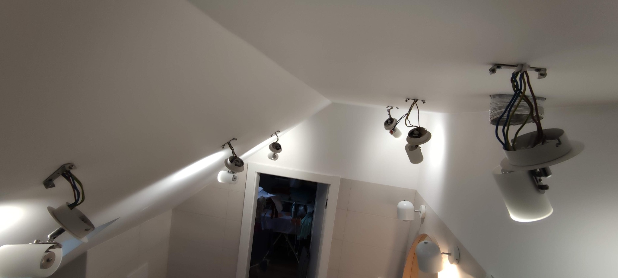 Montaż punktowych lamp sufitowych w łazience na poddaszu, widoczne przewody elektryczne i częściowo zamontowane oprawy oświetleniowe.