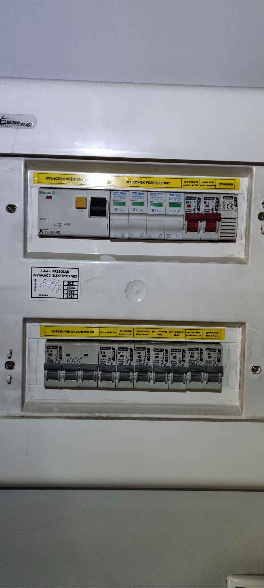 Tablica rozdzielcza z bezpiecznikami i wyłącznikiem różnicowoprądowym, widoczna naklejka z datami przeglądów instalacji elektrycznej.