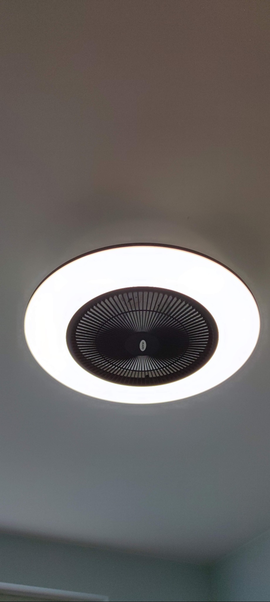 Okrągła lampa sufitowa z wbudowanym wentylatorem, otoczona jasnym, białym światłem LED, zamontowana na gładkim, szarym suficie.