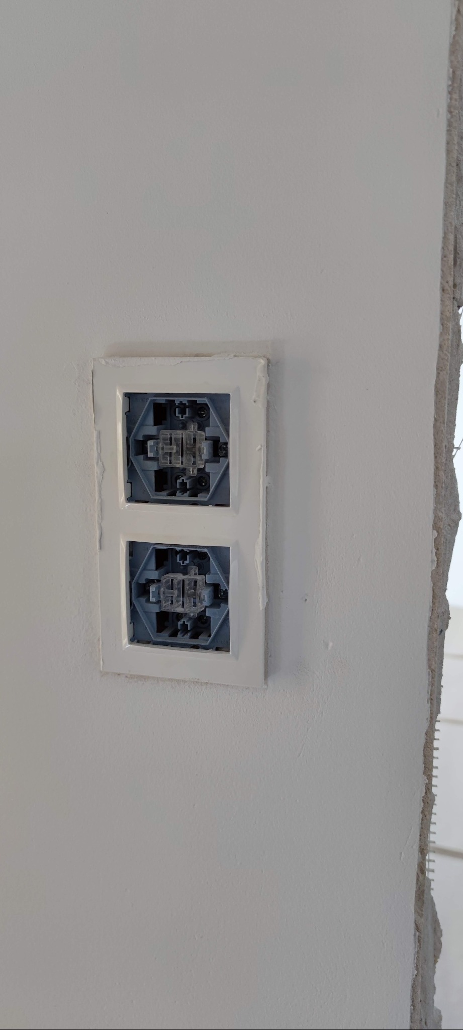 Dwa gniazdka elektryczne bez osprzętu, osadzone w ścianie, z widocznymi śladami świeżo nałożonej gładzi szpachlowej wokół ramek.