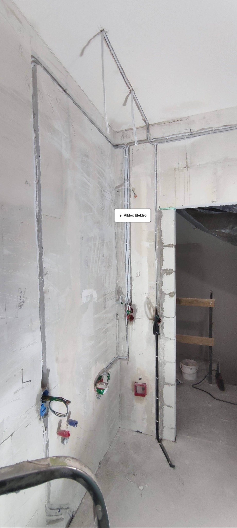 Surowe wnętrze w trakcie prac remontowych: widoczne poprowadzone przewody elektryczne w korytkach na ścianach i suficie, puszki elektryczne, częściowo zabudowane ściany z betonu komórkowego...