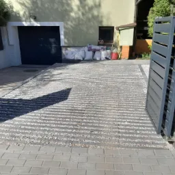 Nowoczesny podjazd z ażurowych płyt betonowych wypełnionych grysem, prowadzący do garażu z automatyczną bramą, widok z poziomu kostki brukowej przy wjeździe.