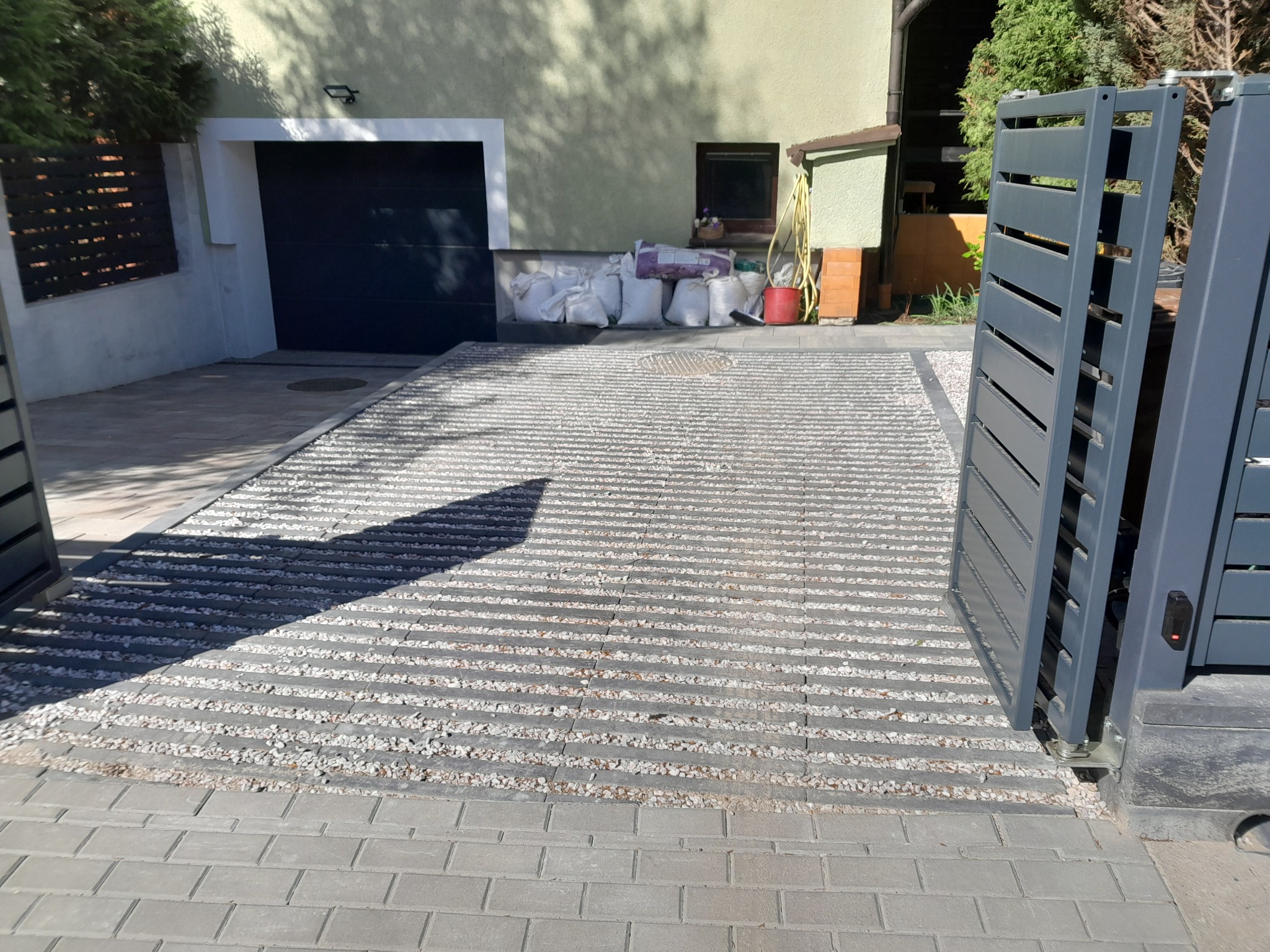 Nowoczesny podjazd z ażurowych płyt betonowych wypełnionych grysem, prowadzący do garażu z automatyczną bramą, widok z poziomu kostki brukowej przy wjeździe.