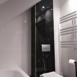 Nowoczesna łazienka w odcieniach bieli i czerni z akcentem złota, ukośna ściana, płytki imitujące marmur, podwieszana toaleta, grzejnik drabinkowy.