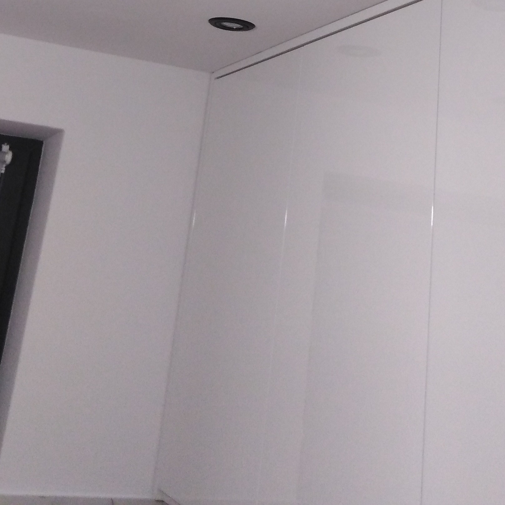 Biała, lakierowana szafa wnękowa z oświetleniem punktowym w suficie, widoczna z perspektywy narożnika pokoju.