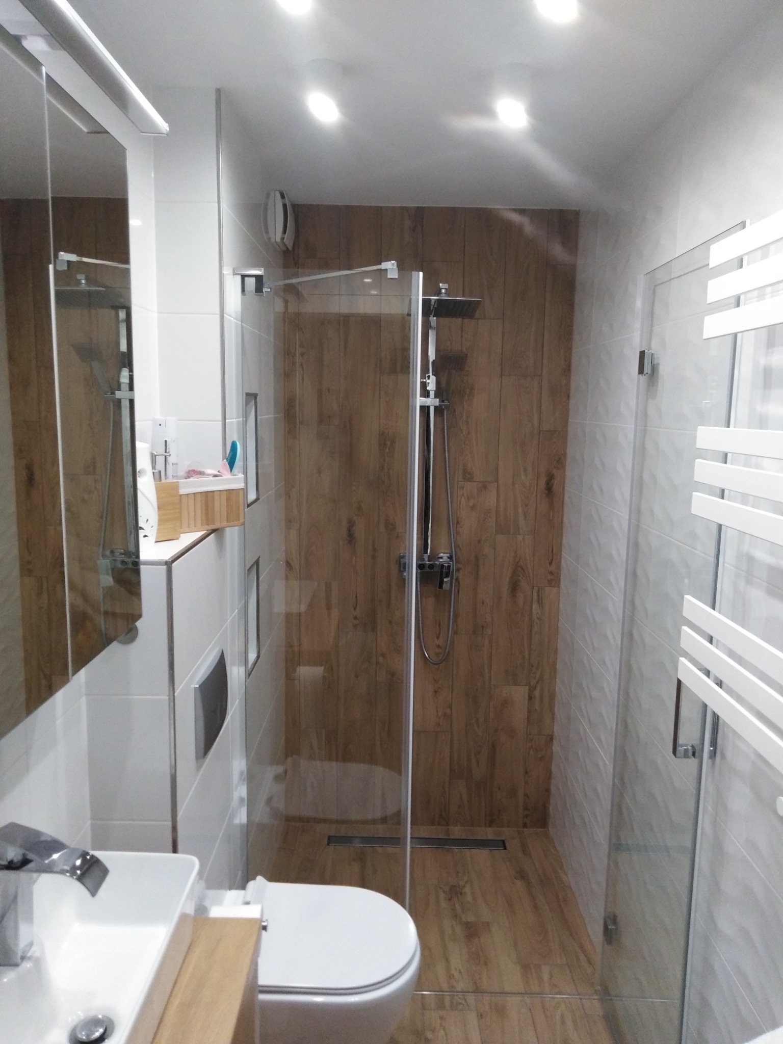 Nowoczesna łazienka z kabiną prysznicową typu walk-in, wykończona płytkami imitującymi drewno, z umywalką nablatową i minimalistyczną armaturą.