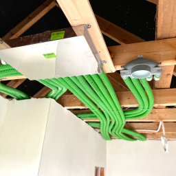 TERMA SYSTEM Patryk Kowalski - Widok z dołu na system rekuperacji z zielonymi przewodami wentylacyjnymi zainstalowany pod drewnianym stropem, widoczny fragment ściany w surowym stanie.