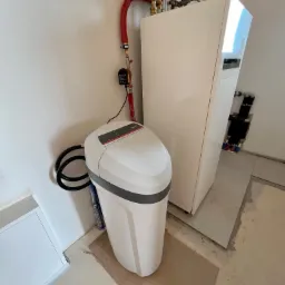 Zmiękczacz wody Viessmann obok białego pieca grzewczego z czerwonymi rurami w nowym pomieszczeniu z surową podłogą.