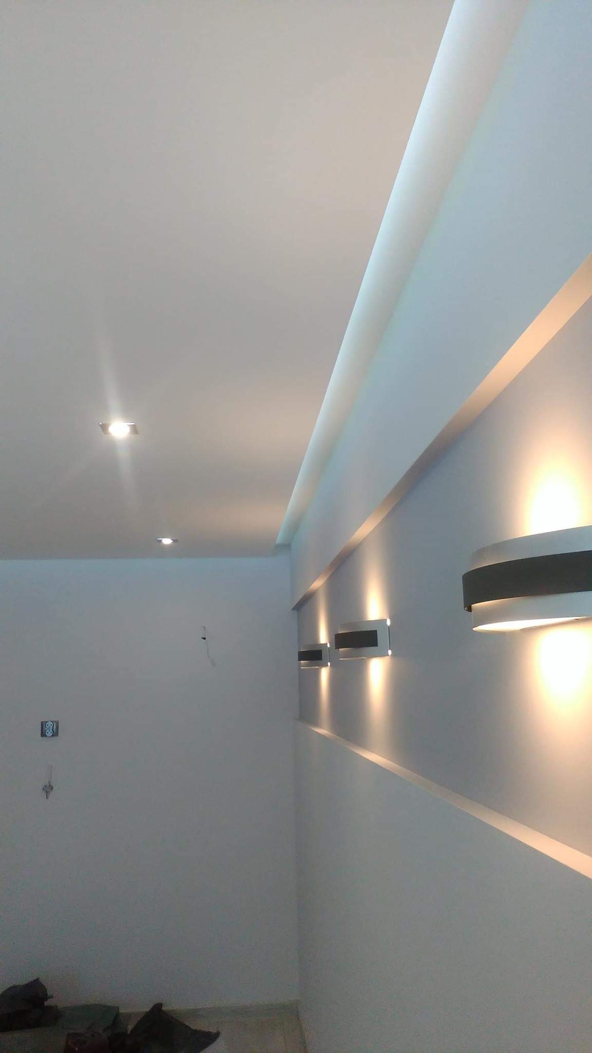 Nowoczesne oświetlenie ścienne i sufitowe w świeżo wykończonym, białym wnętrzu z widoczną listwą przysufitową