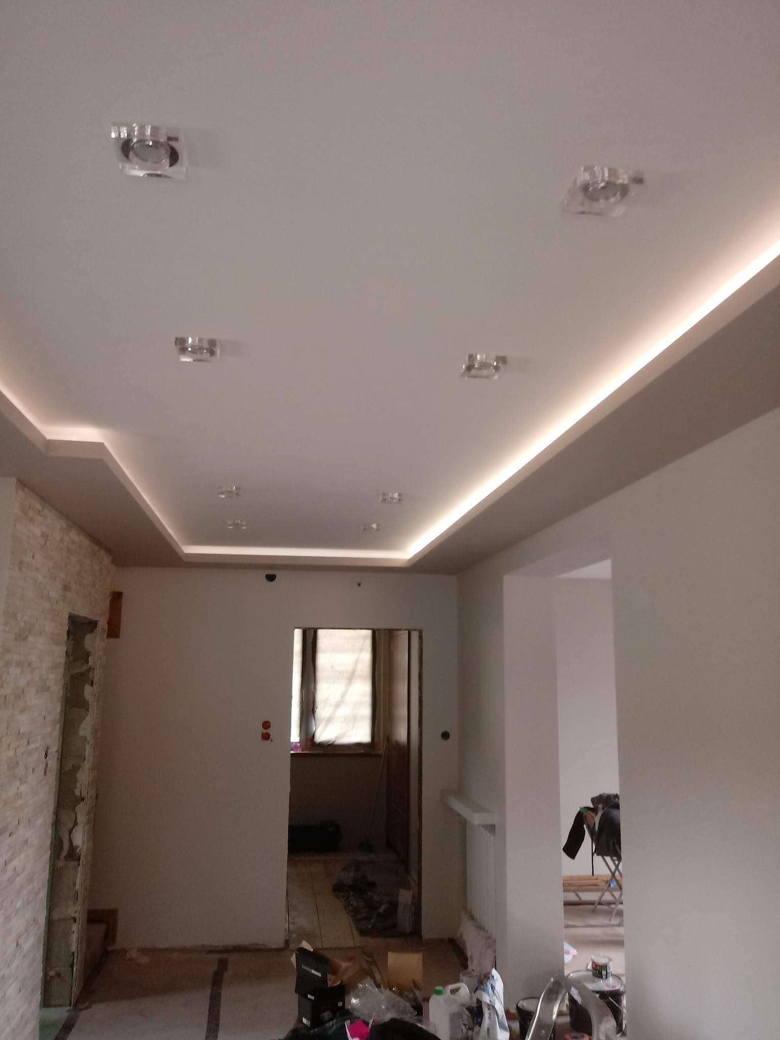 Wykończony sufit podwieszany z oświetleniem LED i punktowymi lampami w mieszkaniu w Łomży, widoczny fragment ściany z imitacją kamienia i przygotowania do dalszych prac wykończeniowych.